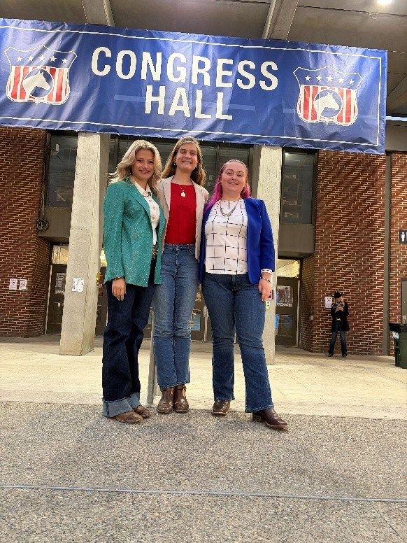 Three smiling young ladies in front of a sign that says Congress Hall.